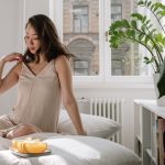 Asian woman in a cozy bedroom enjoying a calm morning with fresh citrus slices on a bed.